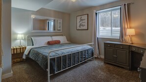 A bedroom with a bed, a nightstand, a dresser, a mirror, and a window with curtains.