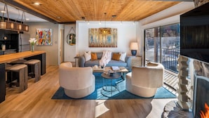 A modern living room with a wooden ceiling, a sofa, two armchairs, a coffee table, and a fireplace.
