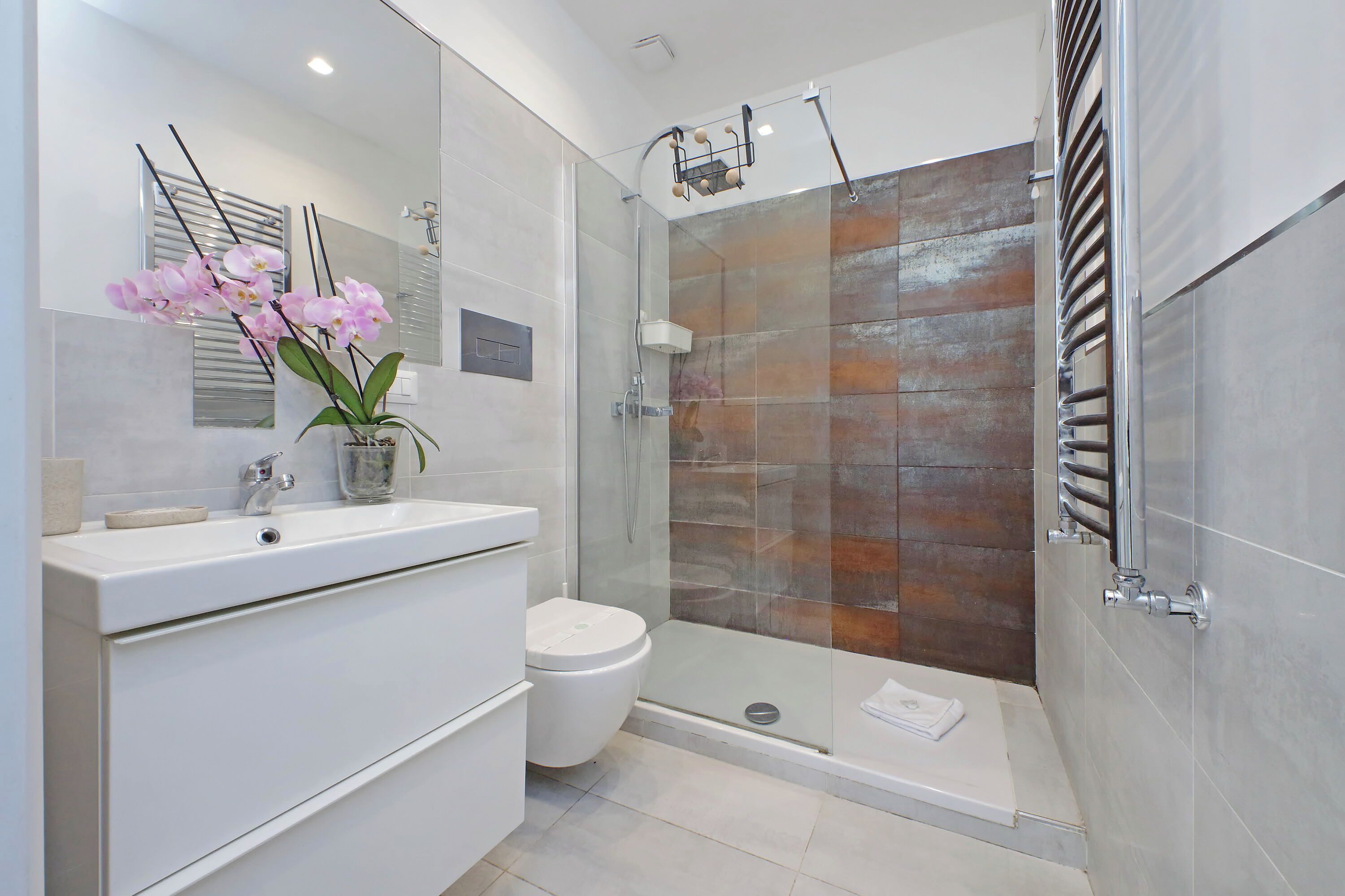 Une salle de bain moderne avec une douche à parois de verre, un lavabo blanc agrémenté d’un vase de fleurs et des toilettes.