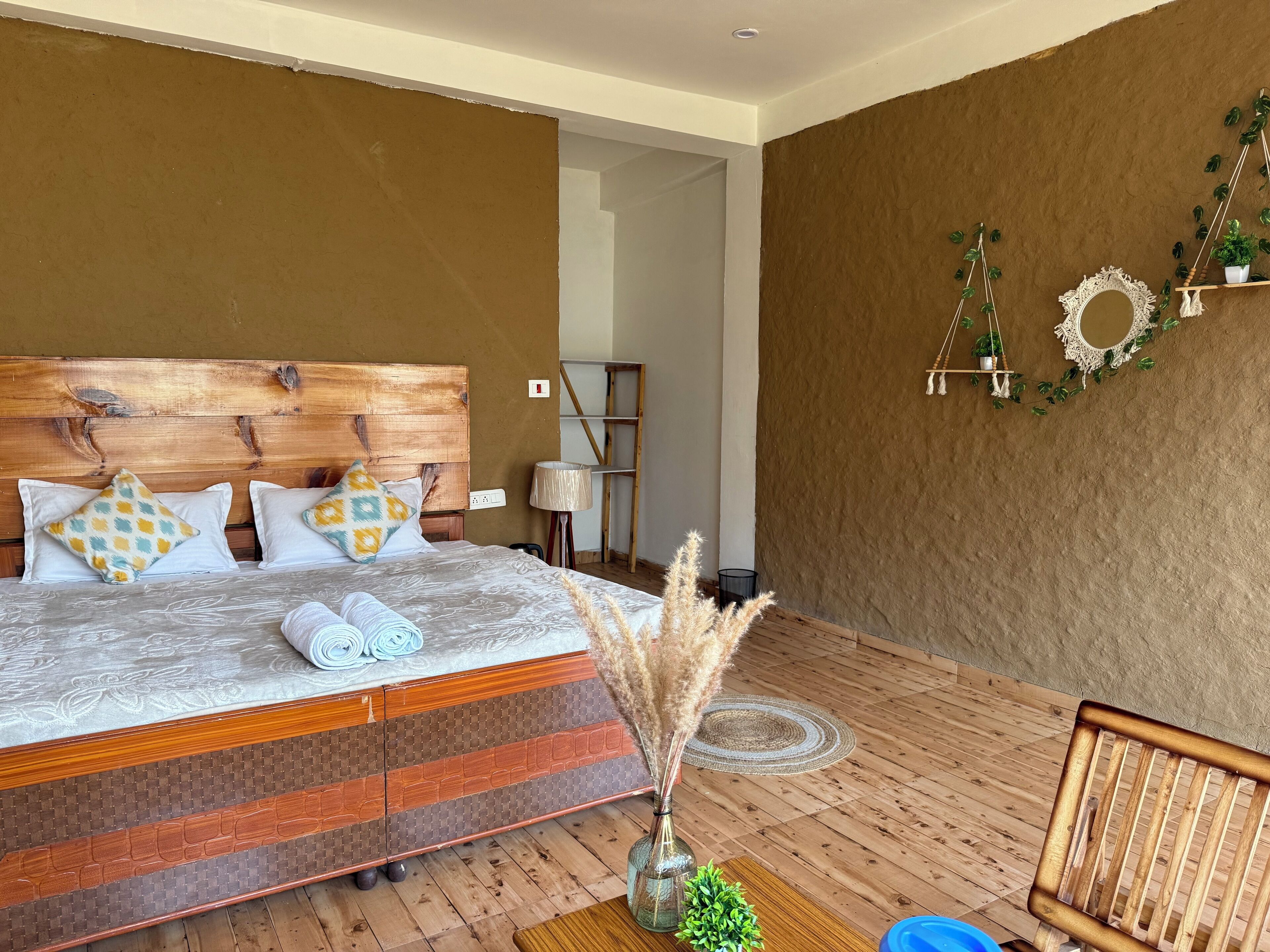 A bedroom with a wooden headboard, patterned bedding, a bedside lamp, and a small plant on the nightstand.