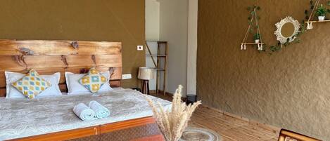 A bedroom with a wooden headboard, patterned bedding, a bedside lamp, and a small plant on the nightstand.