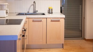 Une cuisine moderne avec des meubles en bois, un évier en acier inoxydable et un luminaire suspendu noir.