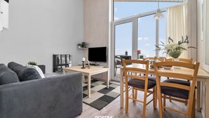 A modern living room with a sofa, TV, and dining area with chairs and a table. - Panorama Dream 47 - Scandinavian, cozy vacation home for 2 to 4 people (St. Andreasberg)
