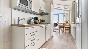 A modern kitchen with white cabinets, a stainless steel range hood, and a dining area with a wooden table and chairs. - Panorama Dream 47 - Scandinavian, cozy vacation home for 2 to 4 people (St. Andreasberg)