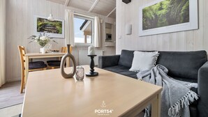 A modern living room with a dark grey sofa, a wooden coffee table, and a dining area with a white table and chairs. - Panorama Dream 47 - Scandinavian, cozy vacation home for 2 to 4 people (St. Andreasberg)