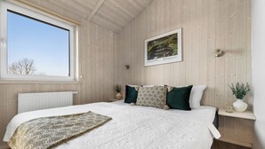 Ein Schlafzimmer mit einem großen Bett, einem Fenster, einem gerahmten Bild und einem kleinen Regal mit einer Pflanze.