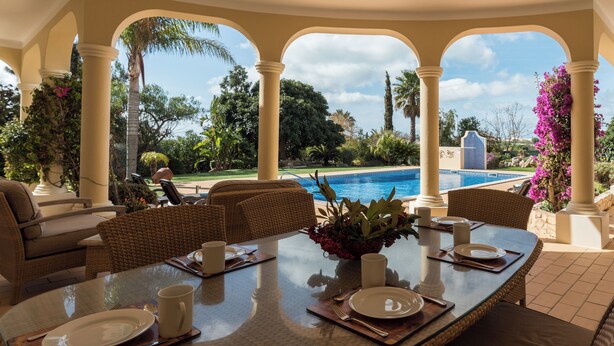 A dining area with a table set for four, overlooking a swimming pool and lush greenery. - Villa Montemar, a 4 bedroom Self Check-in Villa walking distance to Carvoeiro (Carvoeiro)