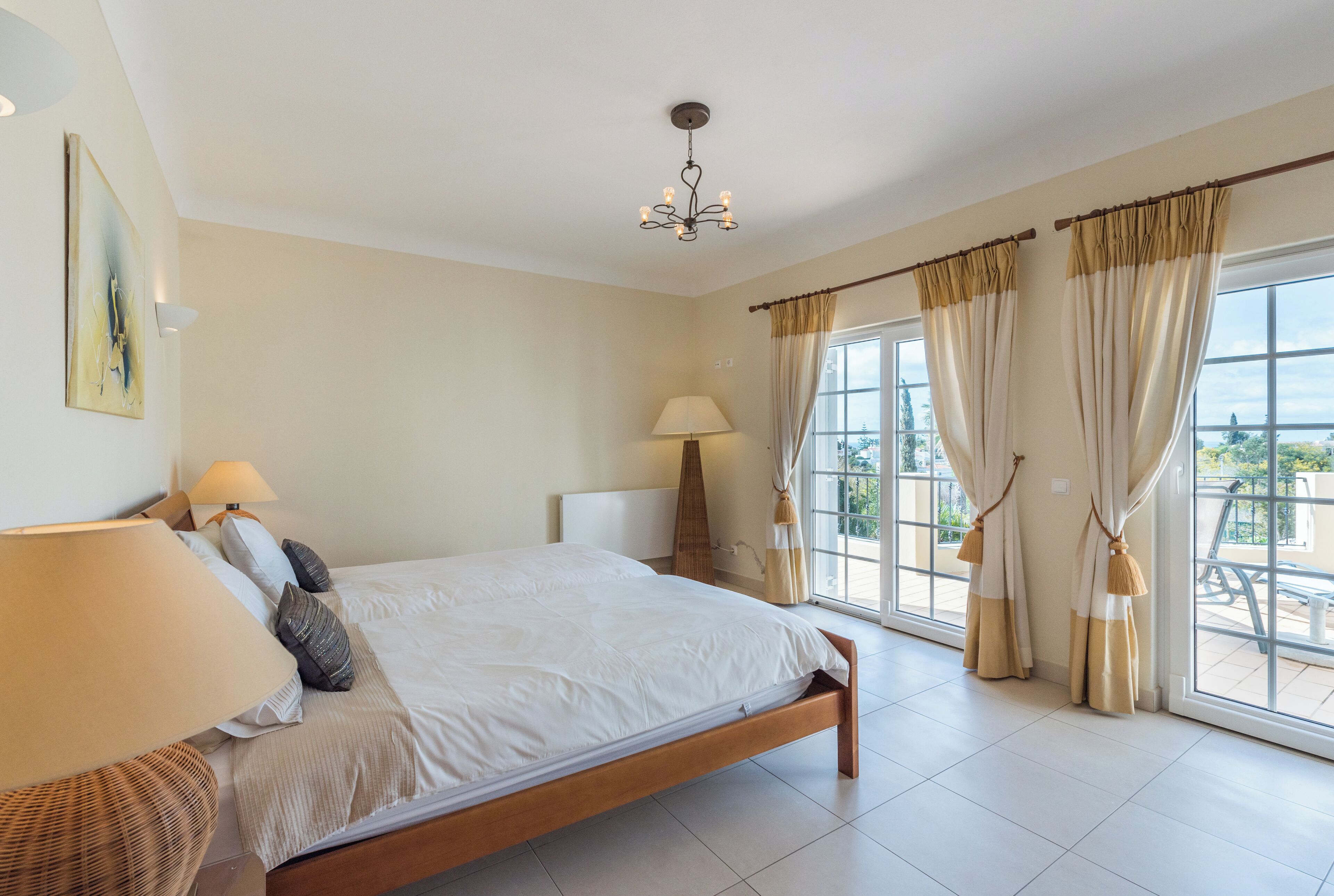 Une chambre à coucher avec un grand lit, un lustre, une fenêtre avec des rideaux et une vue sur l’extérieur.