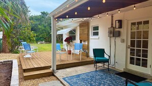 Un patio couvert avec une terrasse en bois, des sièges d’extérieur et une porte donnant sur l’intérieur.