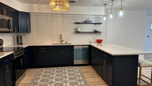Une cuisine moderne avec des meubles de couleur sombre, un pare-feu blanc et un tapis à motifs.