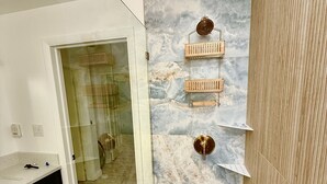 Une salle de bain avec une porte de douche en verre, un mur en marbre et un meuble-lavabo en bois.