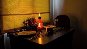 A dining table with plates, cutlery, and a candle, set against a patterned wall and a window with curtains.