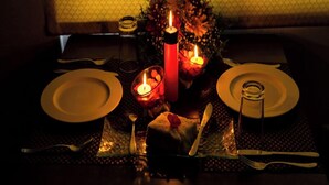 A dimly lit dining table with candles, plates, cutlery, and a glass of water.