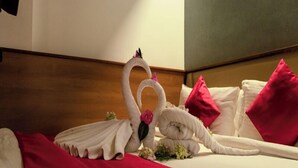 A hotel room with a bed featuring a swan towel arrangement and red pillows.