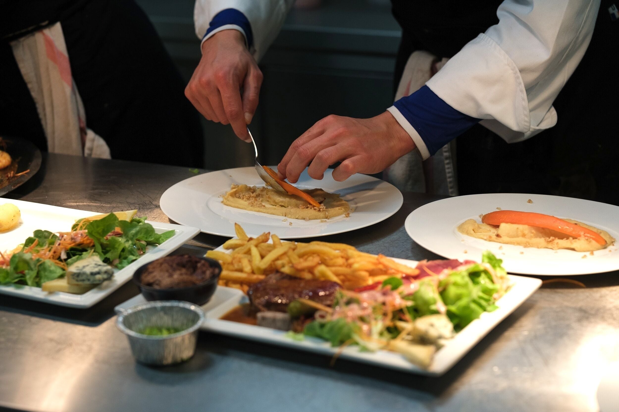 Uma mesa de jantar com diversos pratos, incluindo uma salada, batatas fritas e um bife.