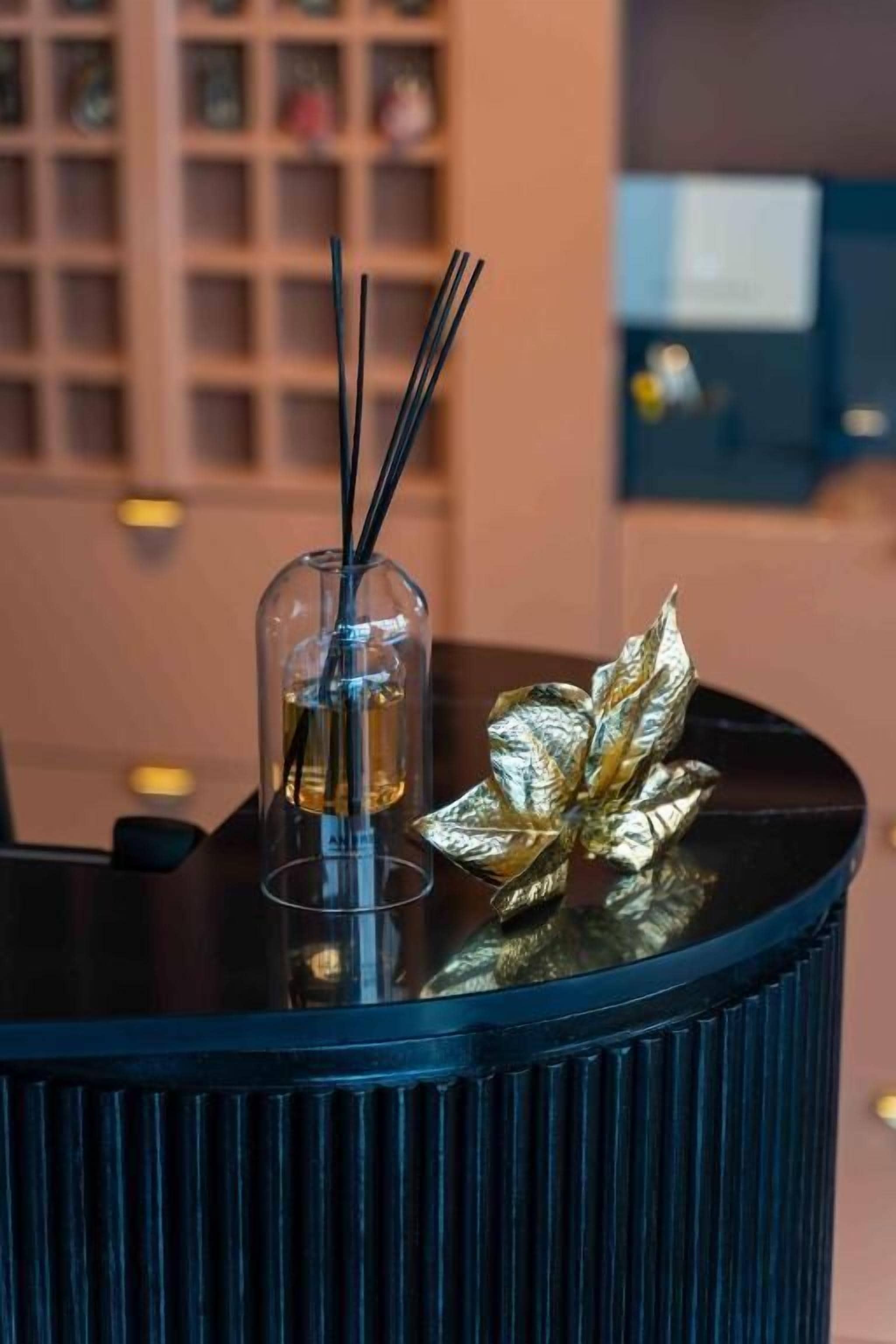 A dark blue, ribbed table with a glass container holding a liquid and two black sticks, and a decorative golden leaf on the table.