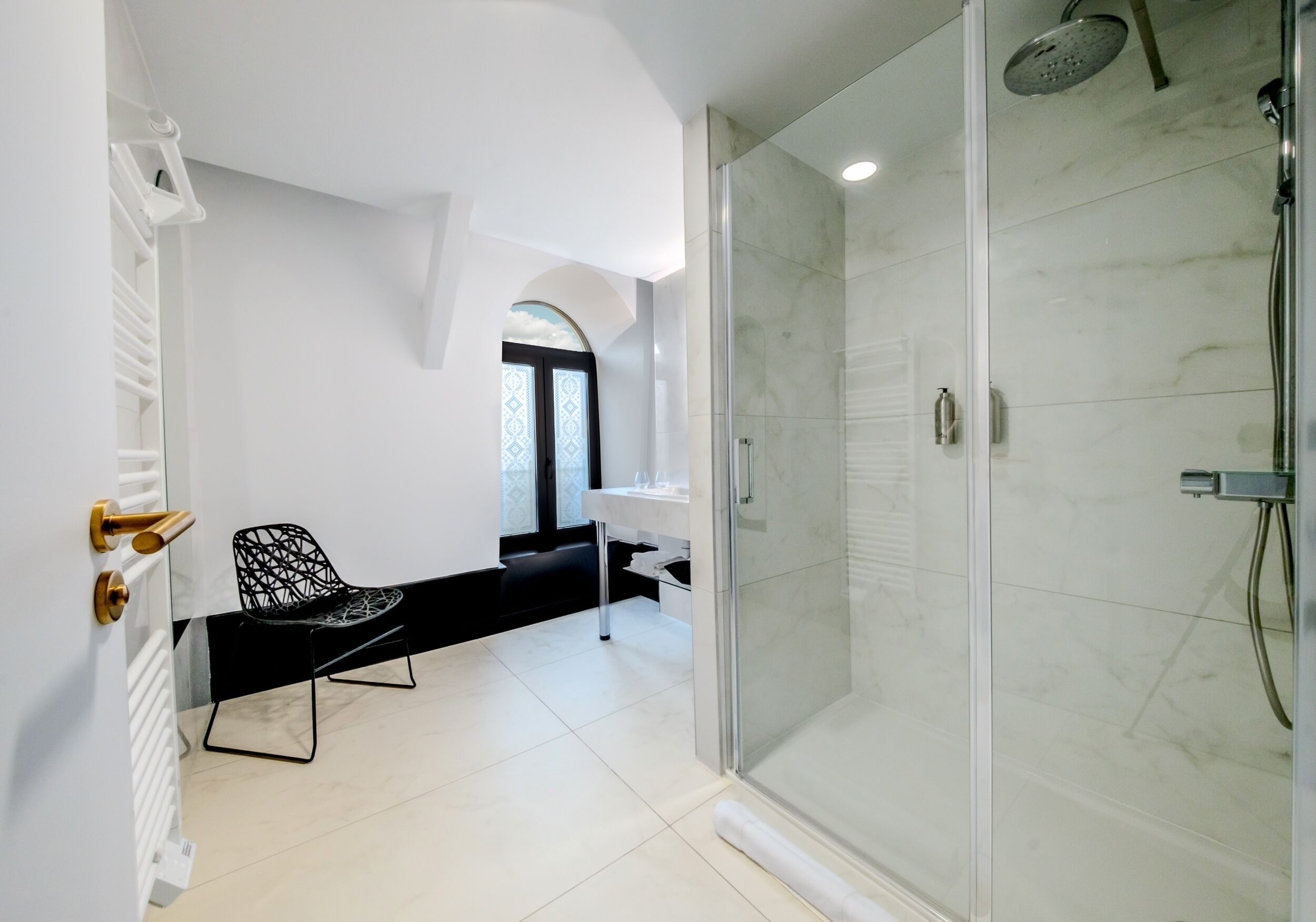 A modern bathroom with a glass-enclosed shower, a black chair, and a white vanity.