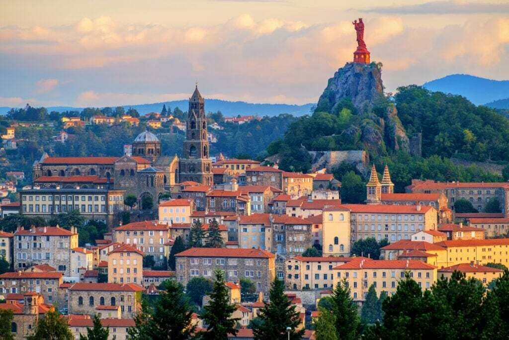 A historic town with a prominent church and a statue on a hill.