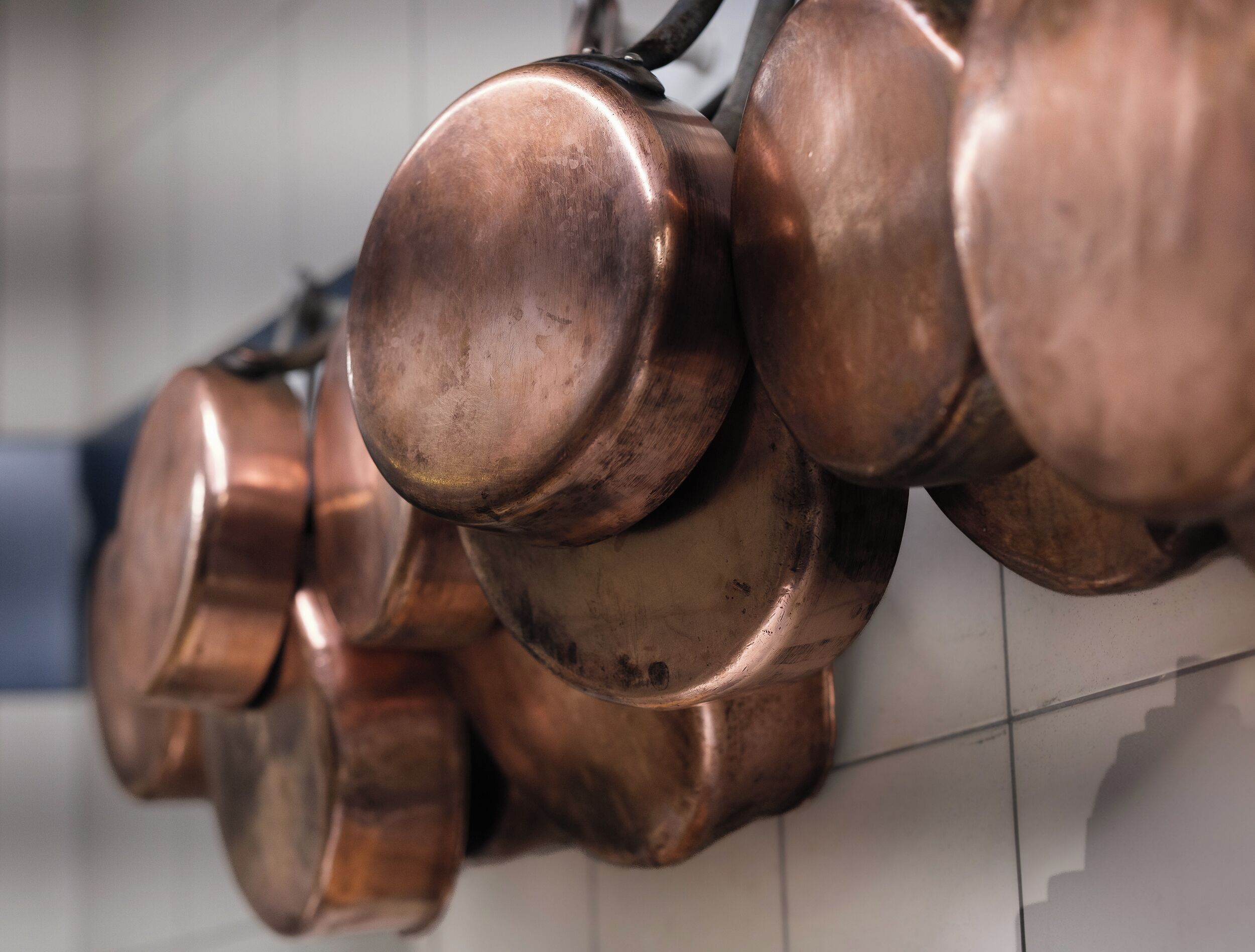 A series of copper pots hanging on a tiled wall.