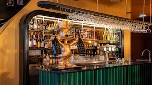 A bar area with a bartender's station, shelves of liquor bottles, and a glassware rack. - Hôtel Le Regina (Le Puy-en-Velay)