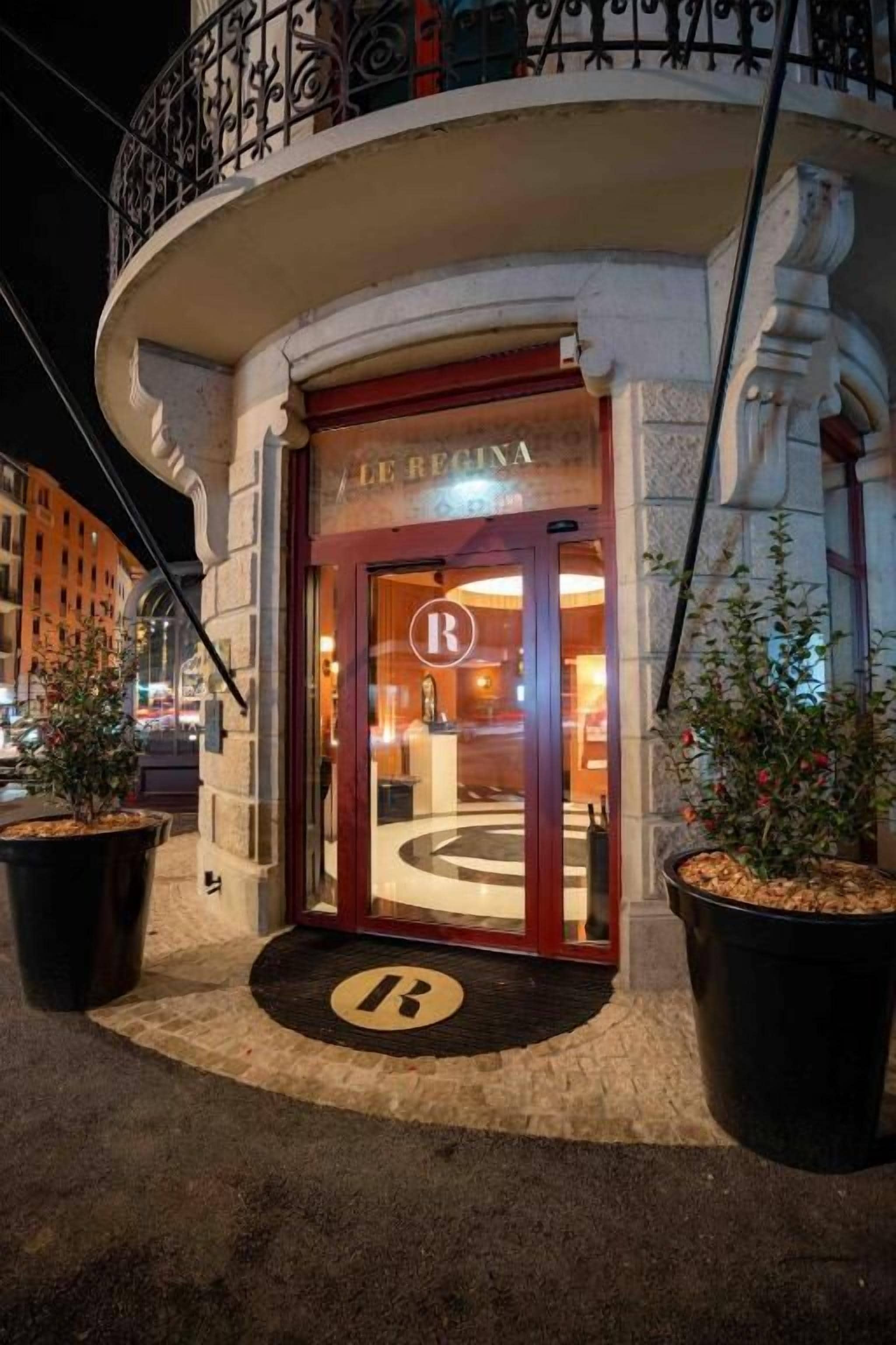 L’entrée d’un hôtel au design classique, avec un logo en forme de « R » bien visible sur la porte et un emblème circulaire sur le sol.