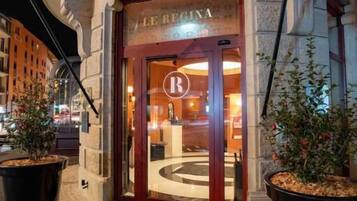 A entrada de um hotel com design clássico, exibindo um logotipo 'R' em destaque na porta e um emblema circular no chão.