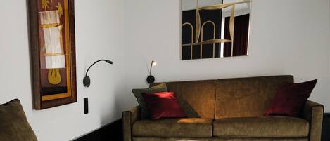 A living room with a sofa, a coffee table, a framed artwork, and a wall-mounted lamp.