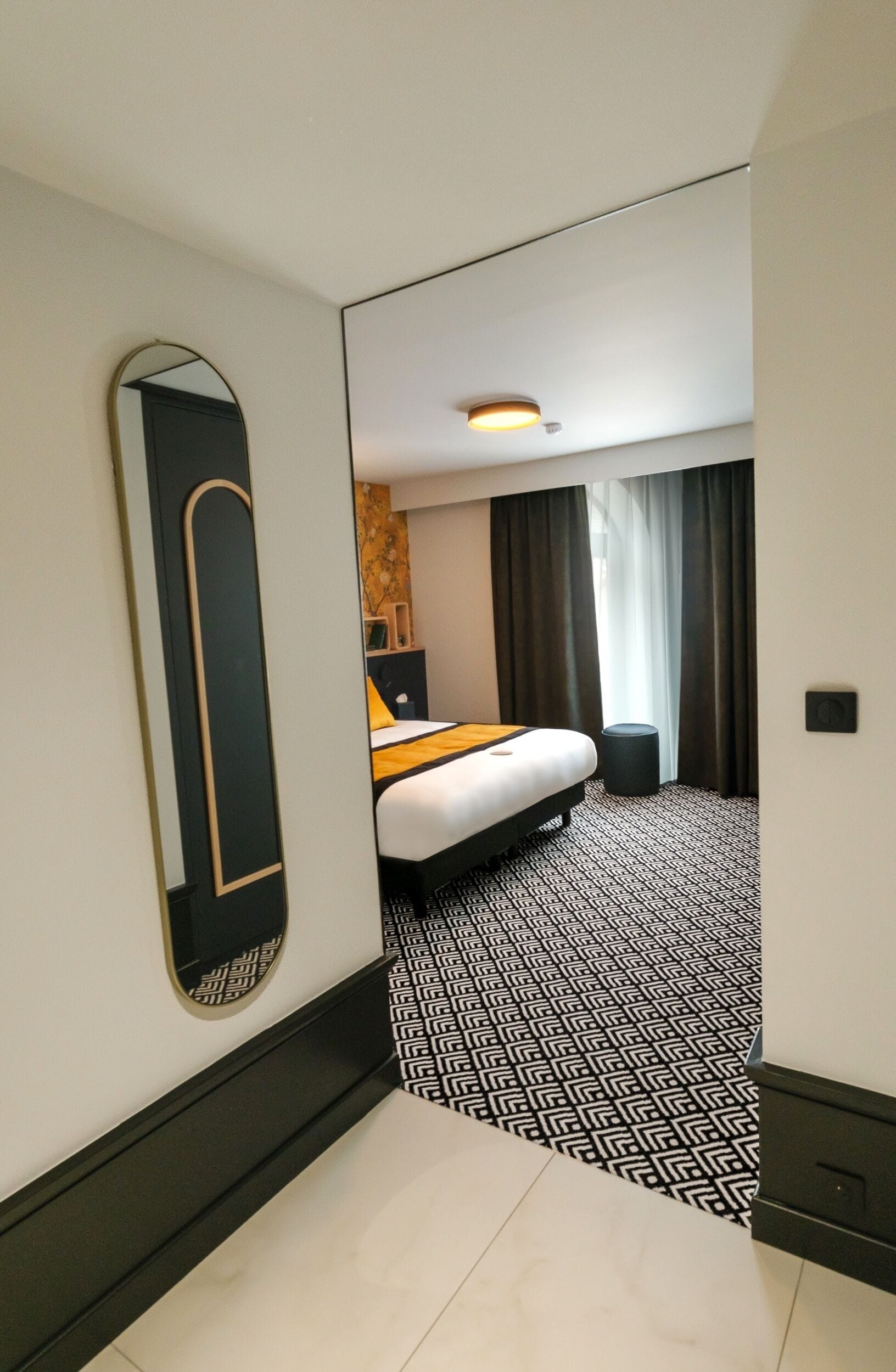Une chambre d’hôtel avec un lit, un miroir, une petite table et une poubelle.