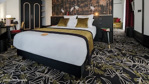 A modern hotel room with a large bed, a desk with a lamp, a bookshelf, and a wall with a nature-themed mural. - Hôtel Le Regina (Le Puy-en-Velay)