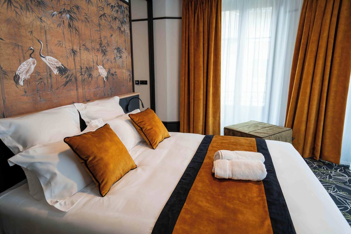 A hotel room with a neatly made bed, a small side table, and a painting on the wall.
