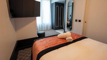 Habitación de hotel con cama, televisor de pantalla plana montado en la pared, armario, espejo y ventana con cortinas.