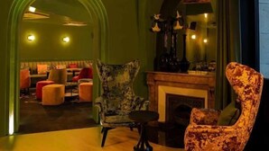 A cozy lounge area with a fireplace, comfortable seating, and a vibrant painting. - Hôtel Le Regina (Le Puy-en-Velay)