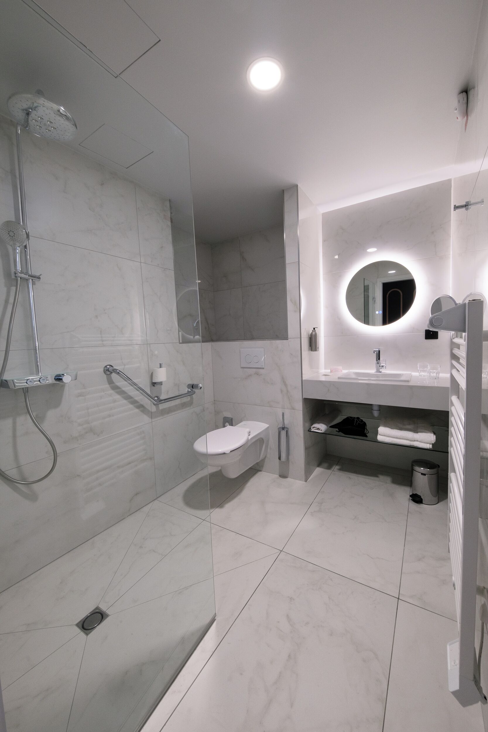Uma casa de banho moderna com chuveiro envidraçado, lavatório branco e espelho com moldura redonda.
