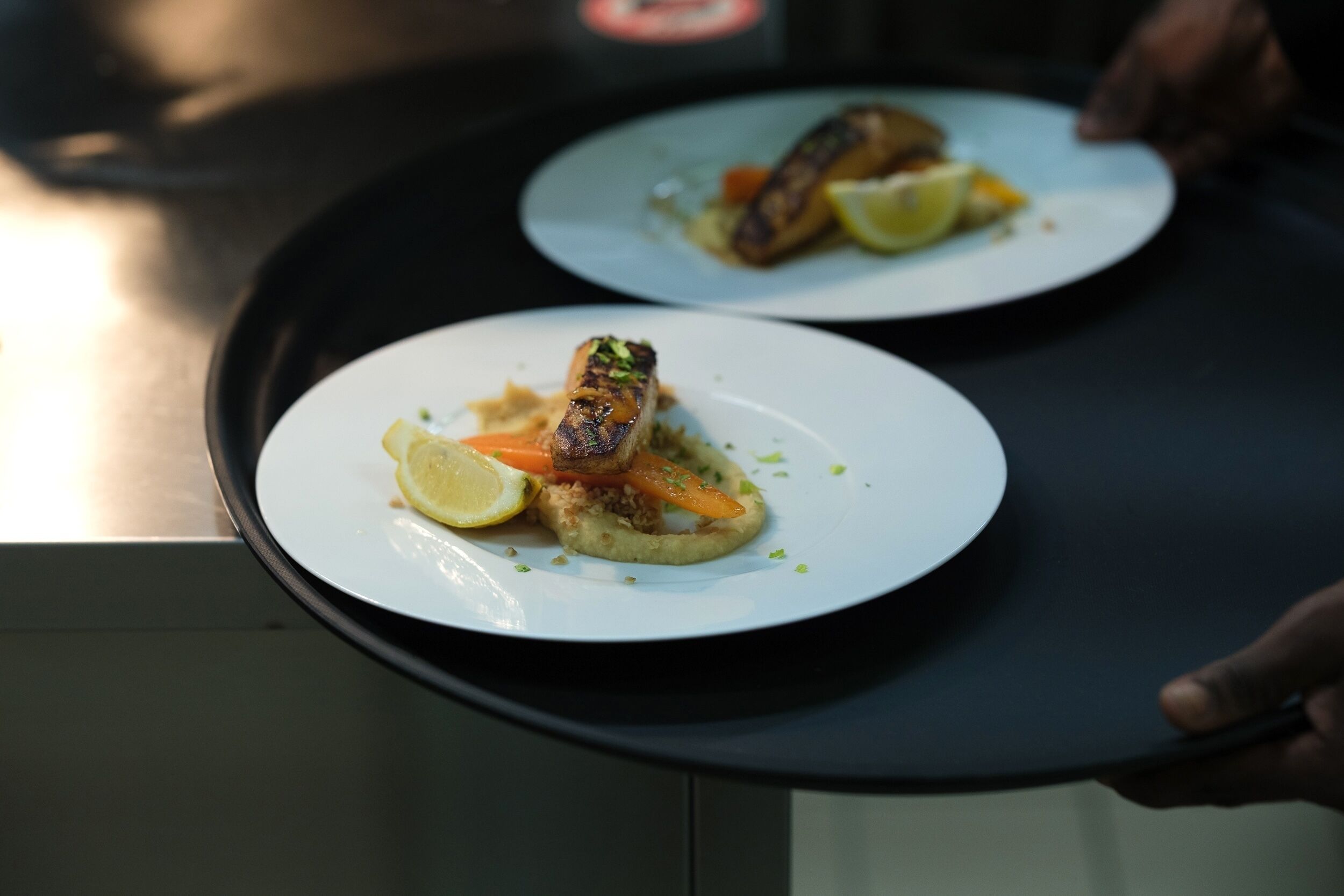 A tray with two plates of food, one with a grilled item and vegetables, and the other with a similar dish.