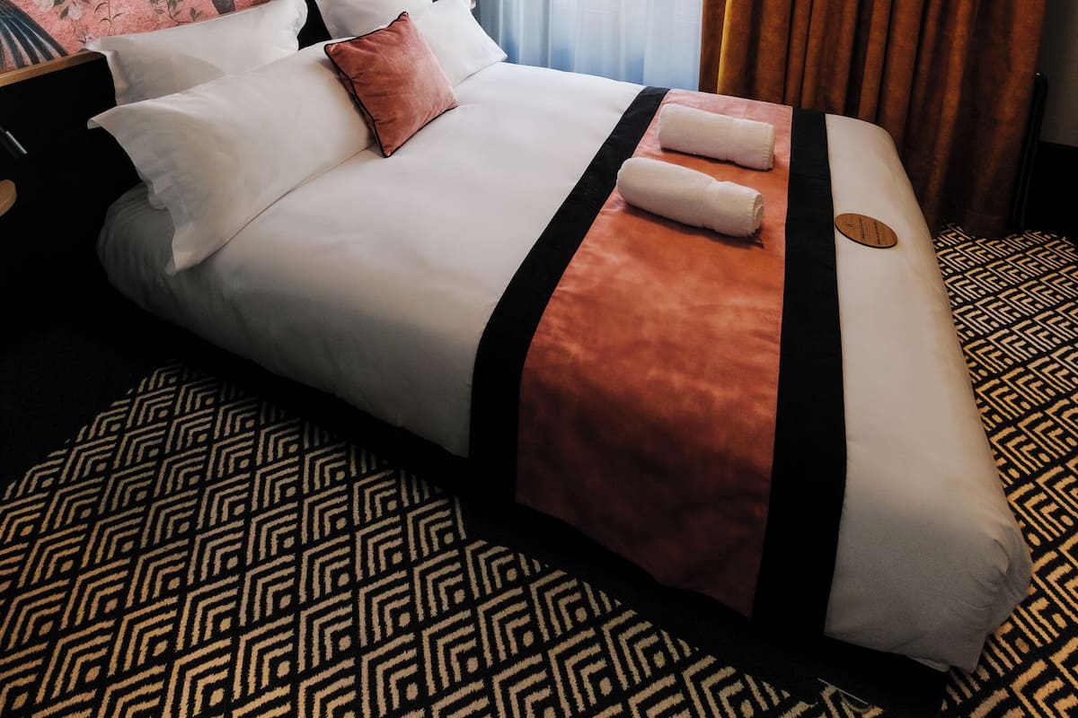 A hotel room with a large bed, a decorative wall mural, a window with curtains, and a patterned carpet.