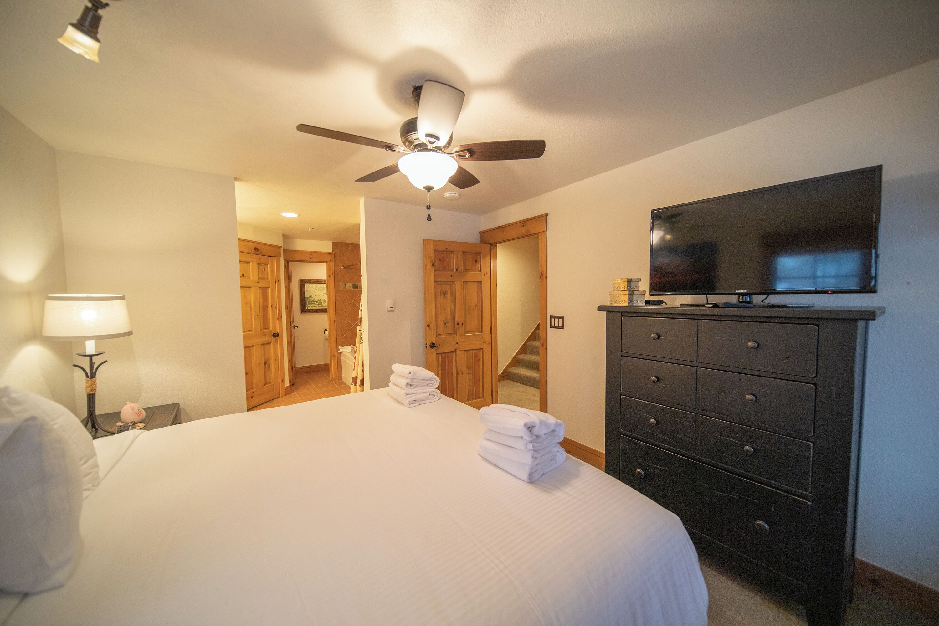 A hotel room with a bed, a ceiling fan, a TV, a dresser, and a lamp.