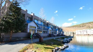 Una fila di edifici moderni a più piani con balconi, un cielo azzurro limpido e un lago calmo.