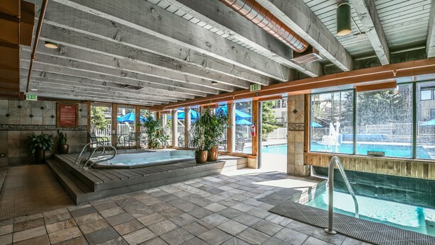 Una piscina interna con soffitto in legno, pavimento piastrellato e piante in vaso.