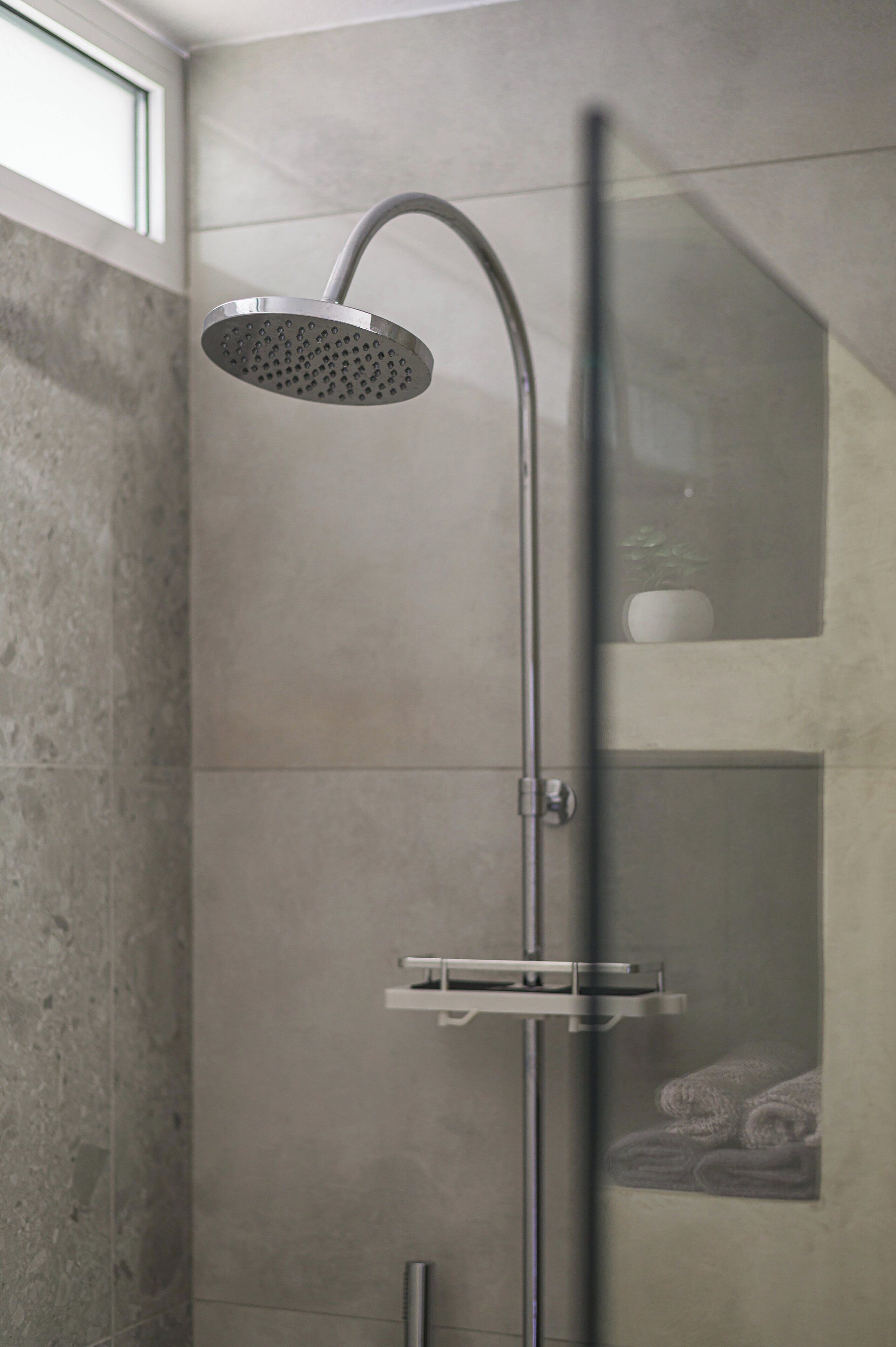 A modern shower with a curved head, a vertical handle, and a glass enclosure.