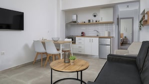 Un salon moderne comprenant un canapé, une table à manger avec des chaises, un coin cuisine avec des placards et des appareils électroménagers, et un téléviseur fixé au mur.