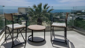 Un balcon avec deux chaises et une table, offrant une vue sur la côte, avec des bâtiments et de la végétation.