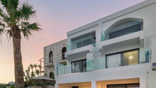 Une maison moderne à deux étages, dotée d’une piscine, d’un espace salon extérieur et d’un palmier.