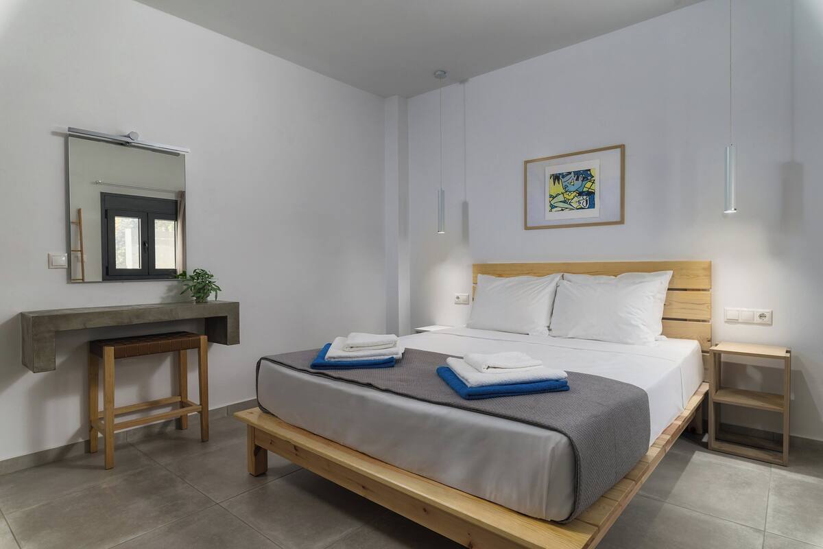 Une chambre à coucher moderne avec un lit, des tables de chevet, un miroir et une œuvre d’art encadrée accrochée au mur.