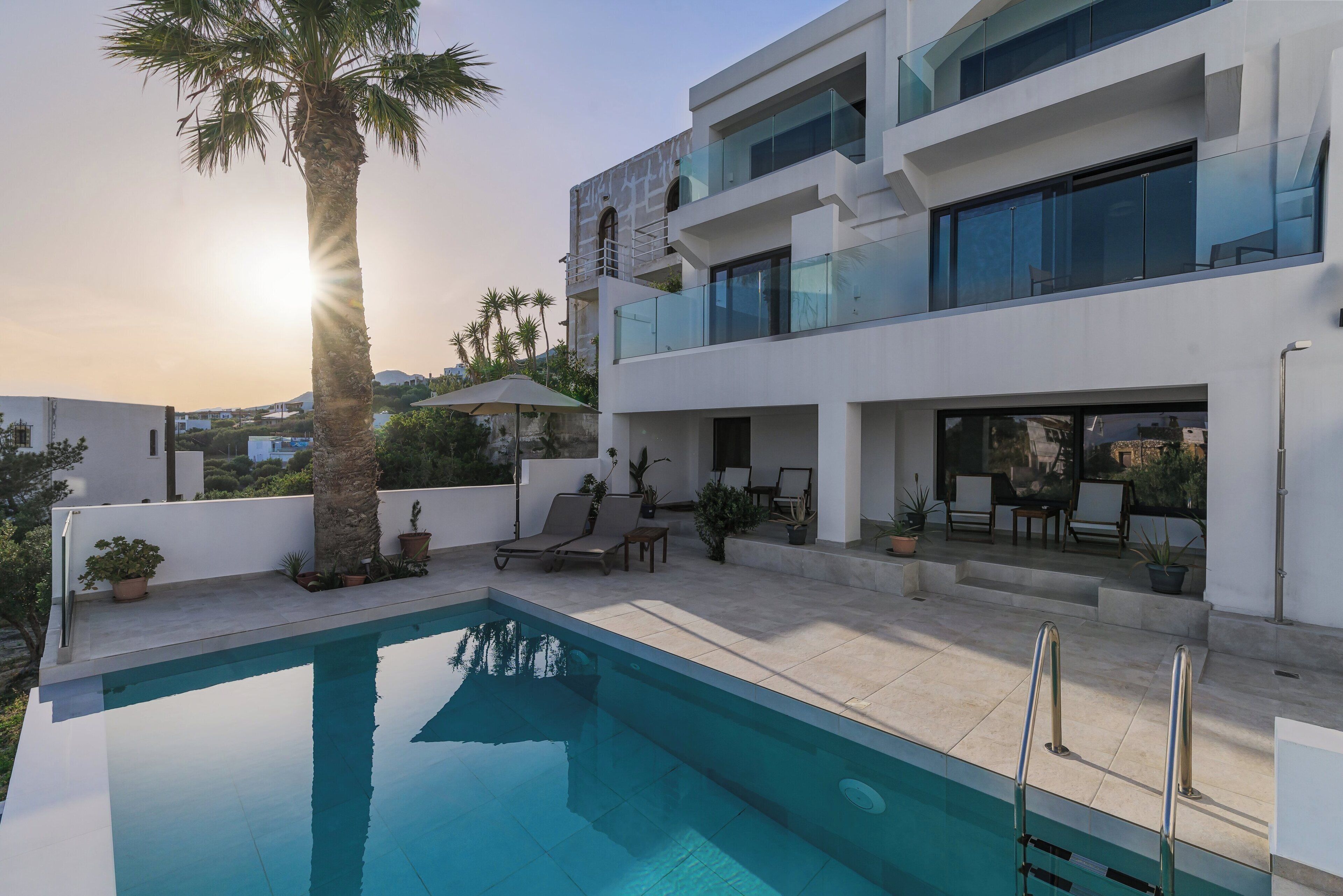 A modern two-story building with a swimming pool, outdoor seating, and a palm tree.