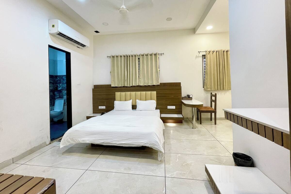 A modern hotel room with a large bed, a bedside table, a chair, a small table, and a built-in sink.