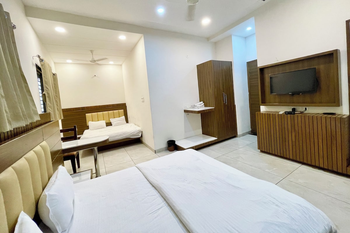 A modern hotel room with a large bed, a TV mounted on the wall, a wardrobe, and a small table.