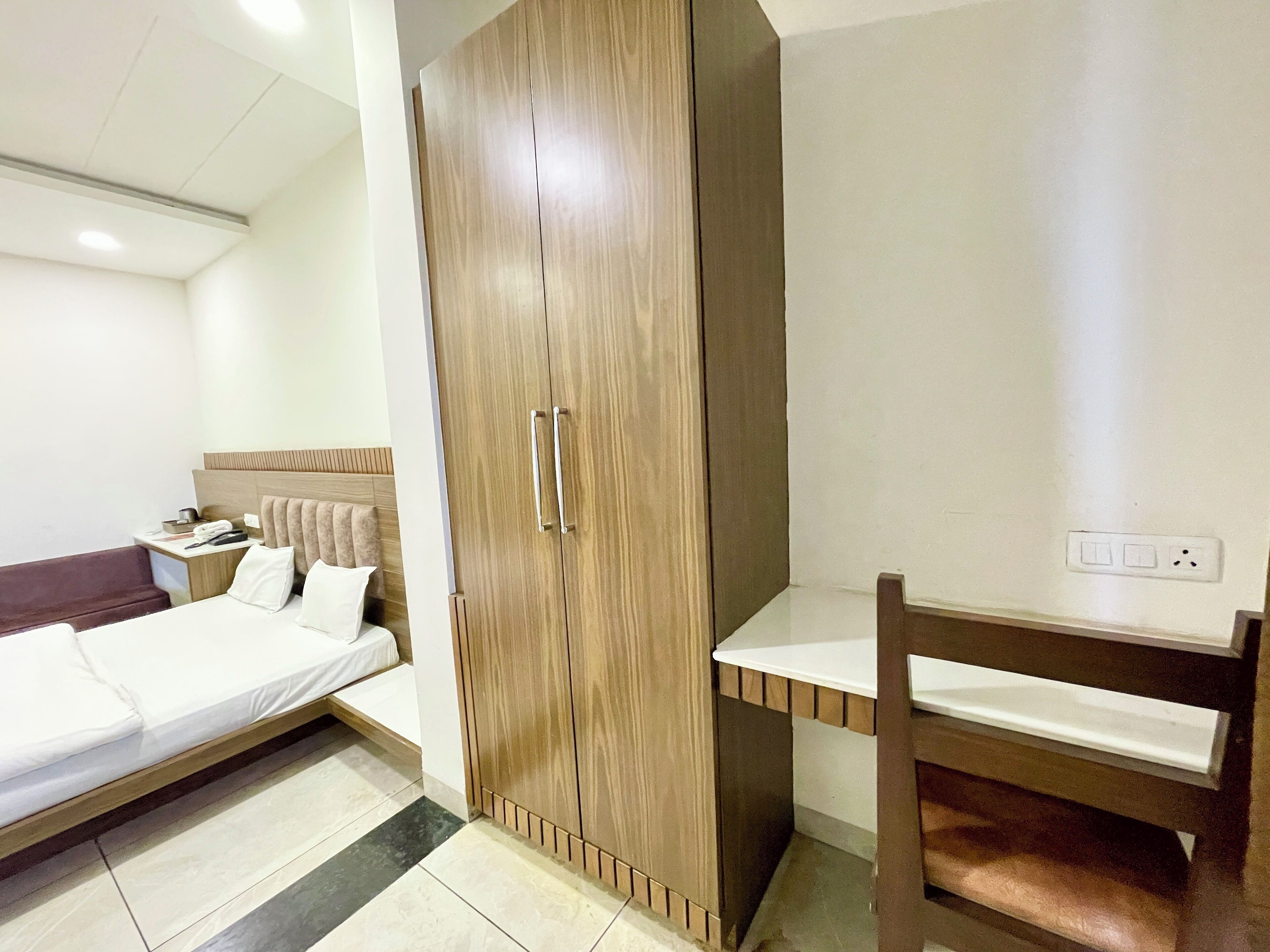 Une chambre d’hôtel comprenant un lit, une armoire en bois, une table de chevet et un bureau avec une chaise.