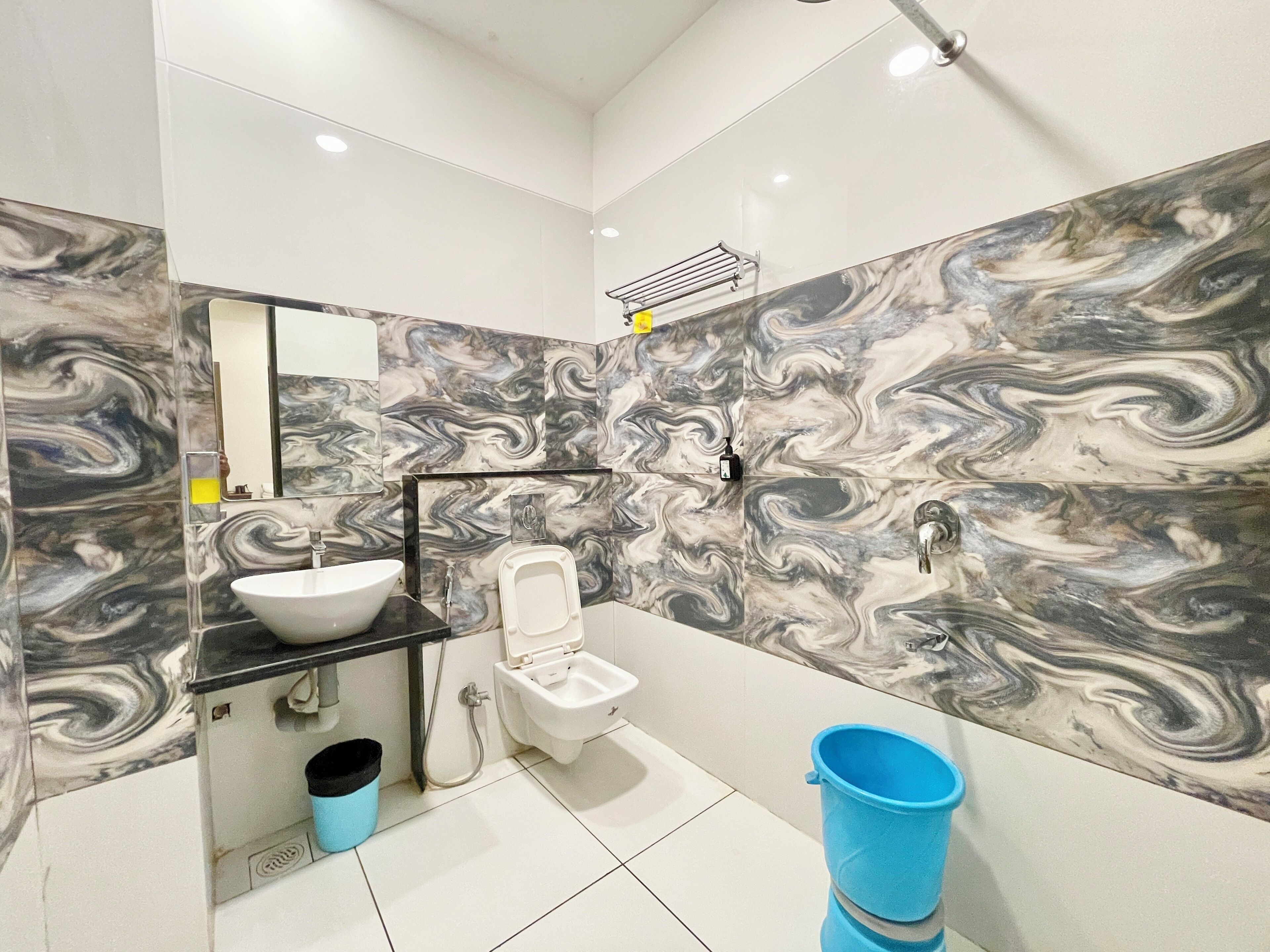 Een moderne badkamer met een marmeren achterwand, een wastafel, een toilet en een blauwe emmer.