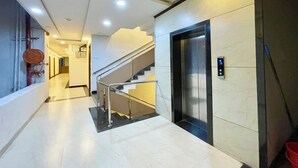 Un moderno vestíbulo de hotel con una escalera de cristal, un ascensor y un piso de baldosas limpias.