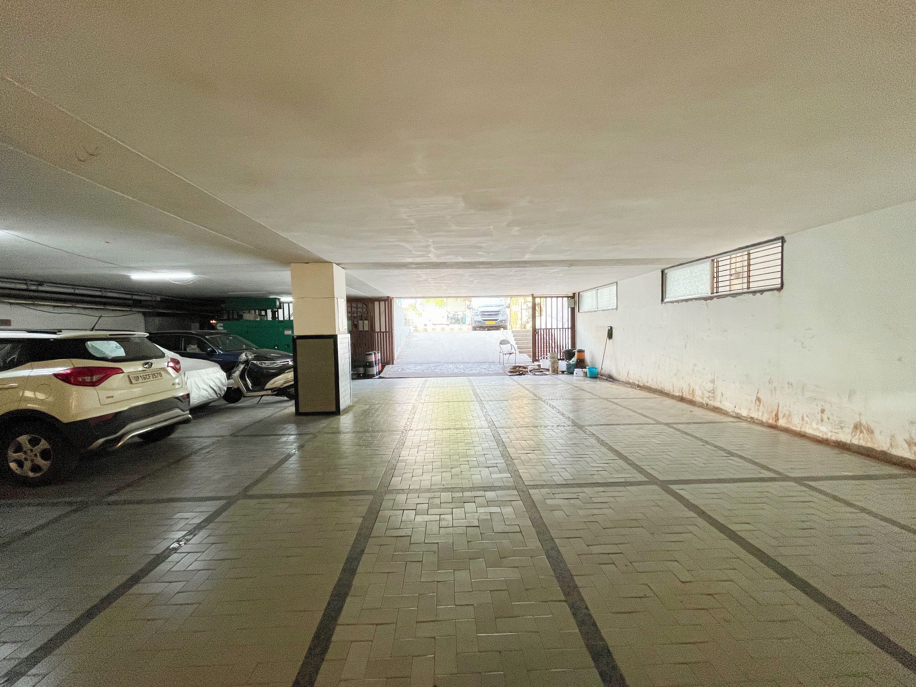 Un parcheggio sotterraneo con auto parcheggiate a sinistra, un cestino dei rifiuti al centro e vista della strada attraverso un portone aperto in fondo.
